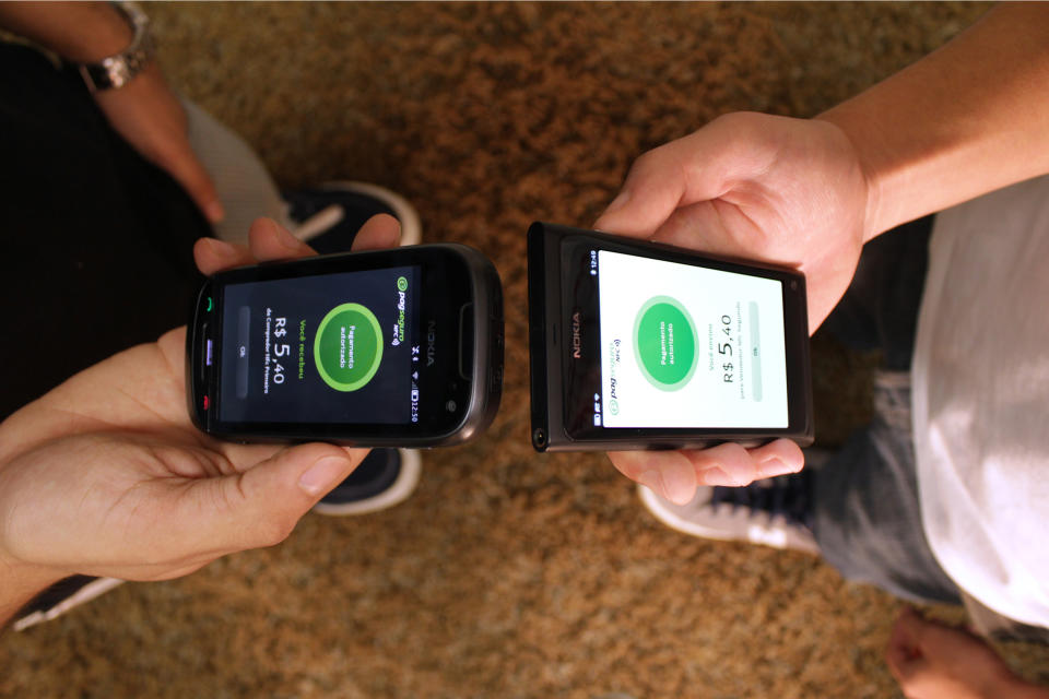 Two people, standing face to face, conducting peer-to-peer payment with their mobile phones.