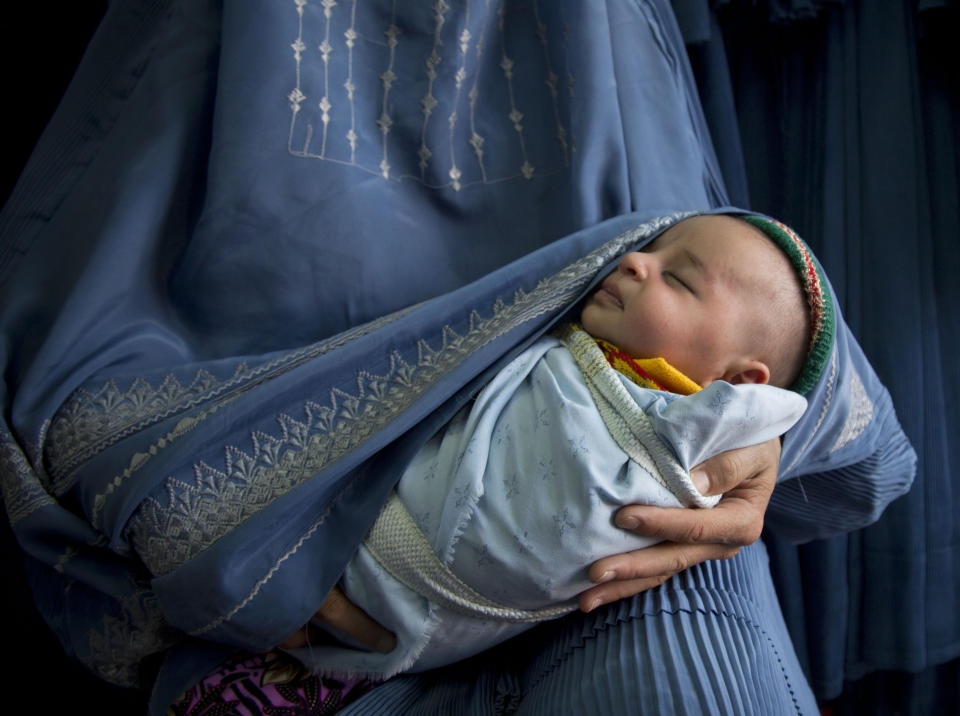 In this Thursday, April 11, 2013 photo, an Afghan woman holds her newly born baby wrapped in her burqa as she waits to get in line to try on a new burqa in a shop in the old town of Kabul, Afghanistan. Despite advances in women’s rights, Afghanistan remains a deeply conservative country and most women continue to wear the Burqa. But tradesmen say times are changing in Kabul at least, with demand for burqas declining as young women going to school and taking office jobs refuse to wear the cumbersome garments. (AP Photo/Anja Niedringhaus)