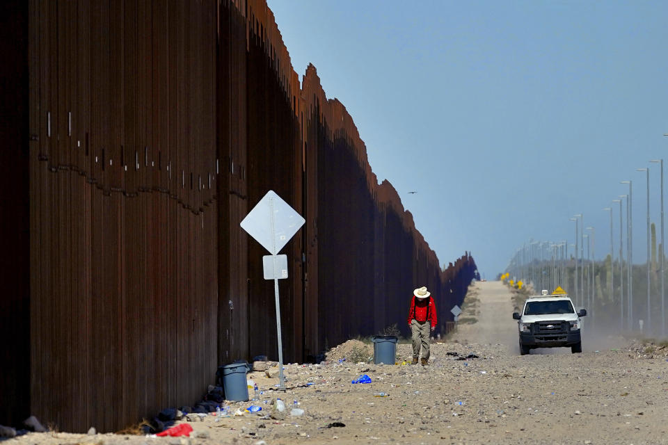 Retired schoolteacher Tom Wingo of Samaritans Without Borders, walks on the Roosevelt Easement picking up trash along the border fence as a U.S. Customs and Border Patrol agent drives patrols the area, Tuesday, Aug. 29, 2023, in Organ Pipe Cactus National Monument near Lukeville, Ariz. U.S. Customs and Border Protection reports that the Tucson Sector is the busiest area of the border since 2008 due to smugglers abruptly steering migrants from Africa, Asia and other places through some of the Arizona borderlands' most desolate and dangerous areas. (AP Photo/Matt York)