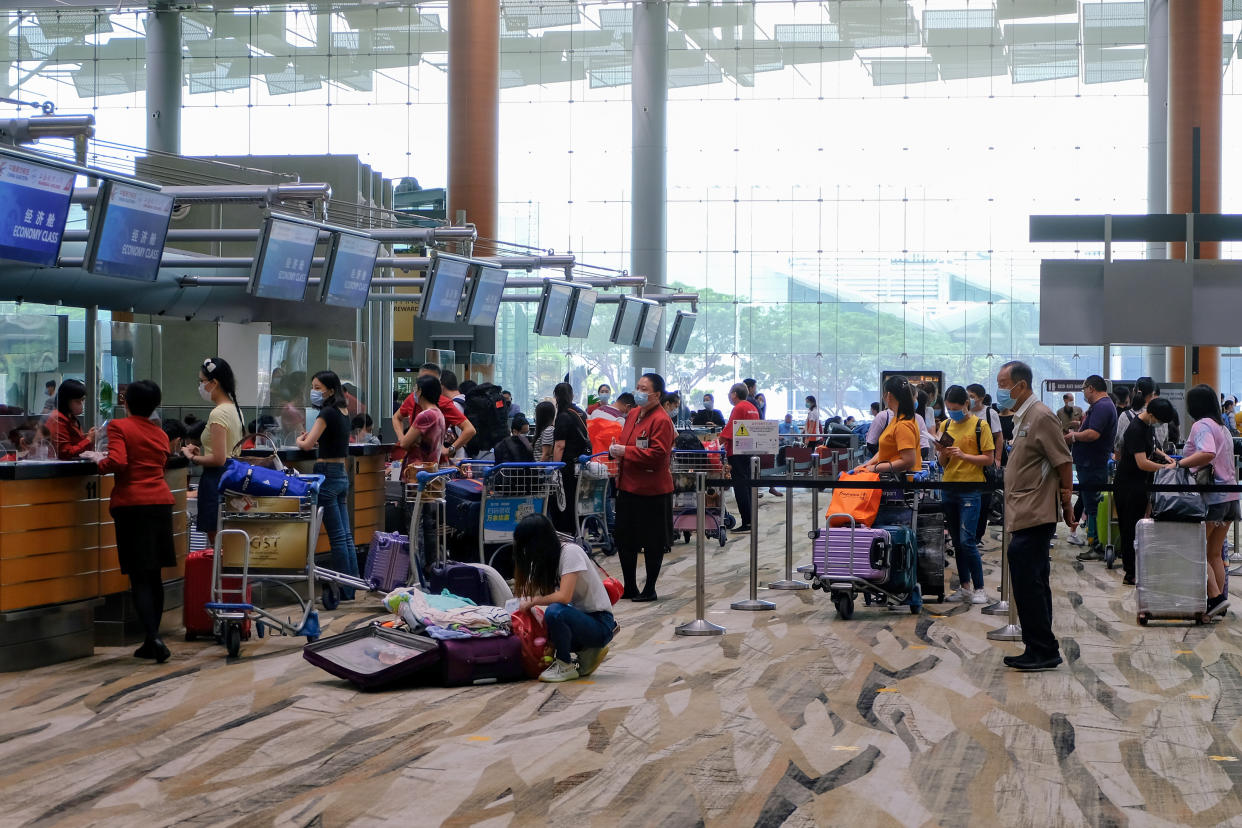 Singapore Jul02 2020 Changi Airport Terminal 3: Travellers returning to their country wait in line to check in at counters; covid-19 Phase 2 reopening. One traveler packing her suitcase in foreground.