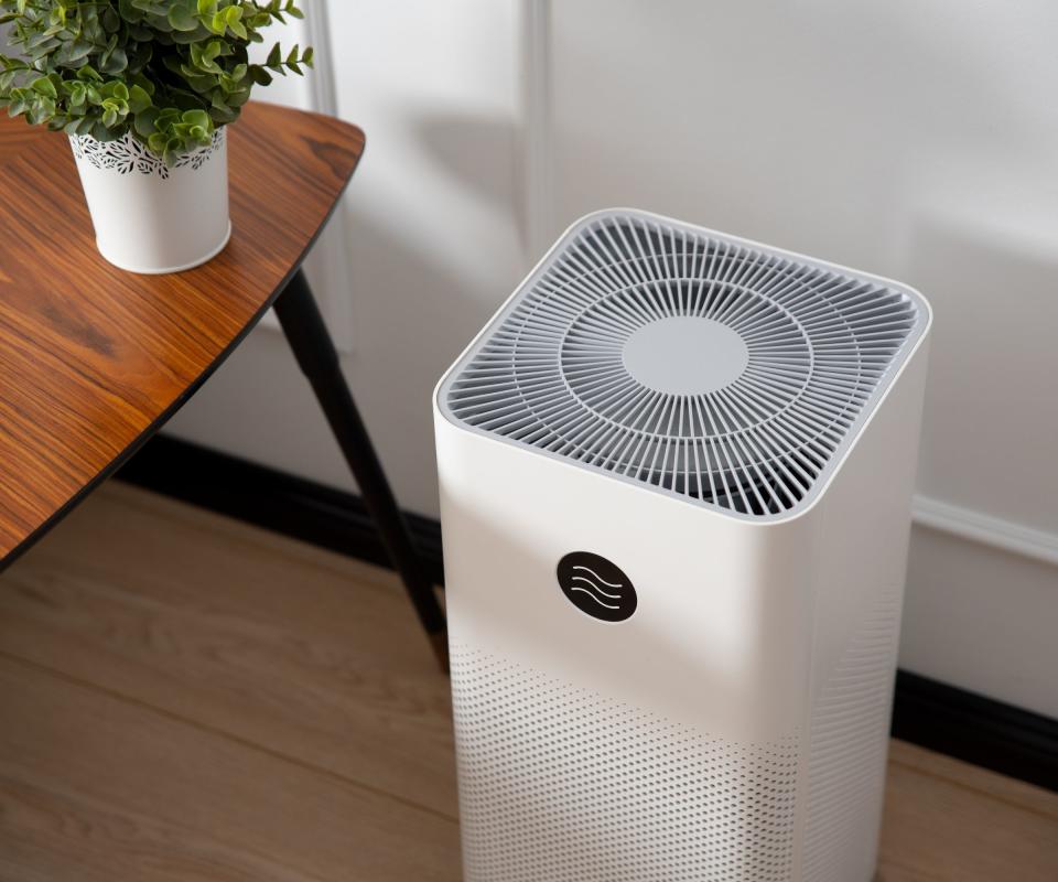 A white air purifer n the floor beside a side table and house plant