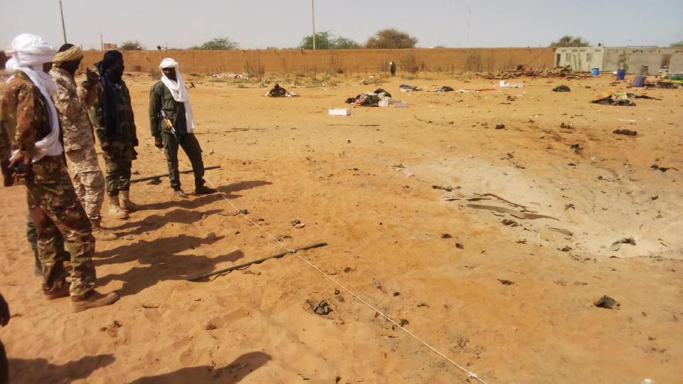Malian troops, left, stand near the scene of an explosion, right, at the Joint Operational Mechanism base in Gao, Mali, Wednesday, Jan. 18, 2017. A suicide bomber in an explosives-laden vehicle attacked a camp in northern Mali on Wednesday, killing more than 50 people and wounding more than 100 soldiers and former fighters now trying to stabilize the region. (AP Photo/Yacouba Cisse)