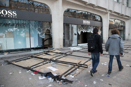 People walk past a damaged Hugo Boss shop on the Champs Elysees avenue during a demonstration by the "yellow vests" movement in Paris, France, March 16, 2019. Picture taken March 16, 2019. REUTERS/Philippe Wojazer