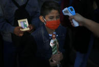A boy holding a statue of Saint Jude and wearing a protective face mask amid the new coronavirus, stands still as his temperature is measured before entering the San Hipolito Catholic church, during the annual pilgrimage honoring Jude, the patron saint of lost causes, in Mexico City, Wednesday, Oct. 28, 2020. Thousands of Mexicans did not miss this year to mark St. Jude's feast day, but the pandemic caused Masses to be canceled and the rivers of people of other years were replaced by orderly lines of masked worshipers waiting their turn for a blessing. (AP Photo/Marco Ugarte)