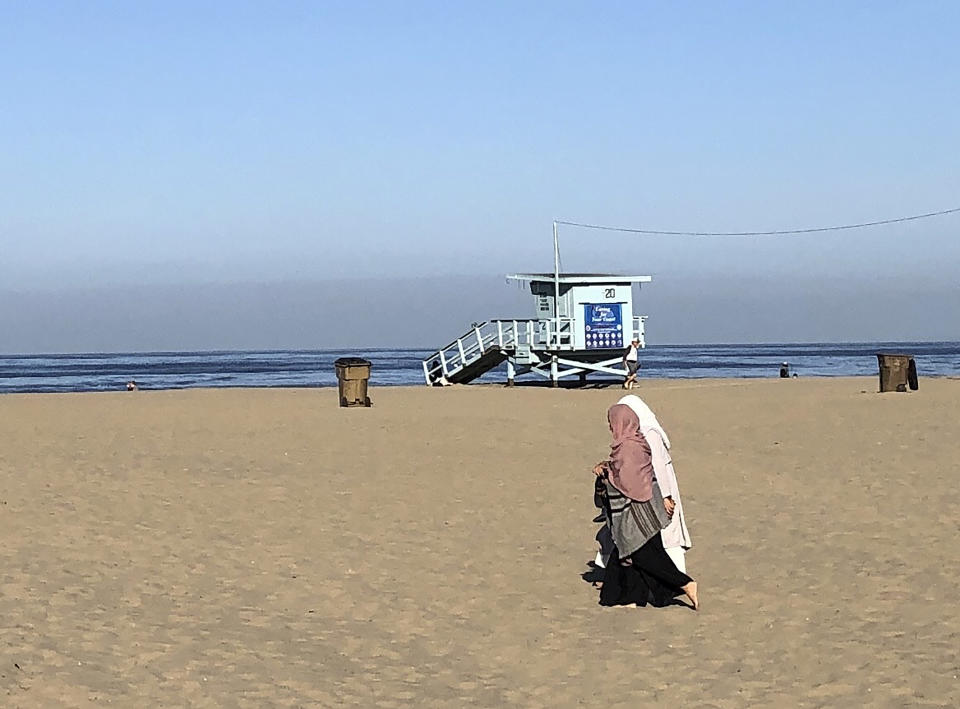 In this Thursday, May 14, 2020, photo, Danyah Alhajri, left, and Mlak Sahli, right, students from Saudi Arabia, walk on Santa Monica beach in Santa Monica, Calif. Masks are required at Los Angeles County beaches, which reopened Wednesday to join counterparts in other states that have allowed a somewhat limited return to famed stretches of sand. (AP Photo/Brian Melley)