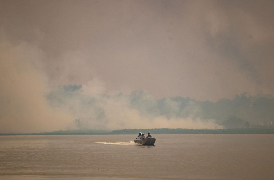 A boat travels at the Encontro das Aguas park as fire consumes an area at the Pantanal wetlands near Pocone, Mato Grosso state, Brazil, Saturday, Sept. 12, 2020. Wildfire has infiltrated the state park, an eco-tourism destination known for its population of jaguars. (AP Photo/Andre Penner)