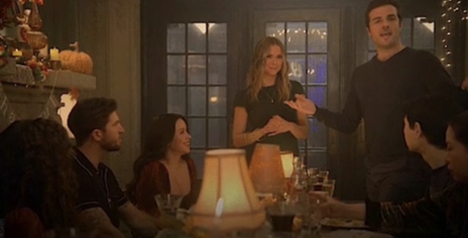 people gather around a dinner table with a man standing, giving a toast