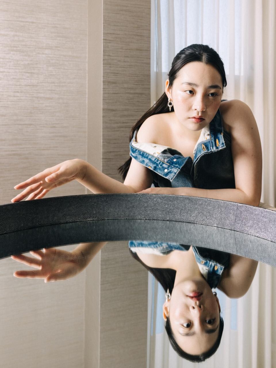 A woman with a dull denim outfit poses for a photo with a mirror.