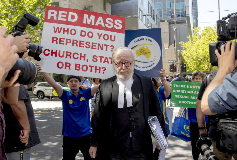 Cardinal George Pell's lawyer Robert Richter leaves the County Court as protesters hold placards in Melbourne, Australia, Wednesday, Feb. 27, 2019. The most senior Catholic cleric ever convicted of child sex abuse could face his first night in custody after a sentencing hearing Wednesday that will decide his punishment for molesting two choirboys in a Melbourne cathedral two decades ago. (AP Photo/Andy Brownbill)