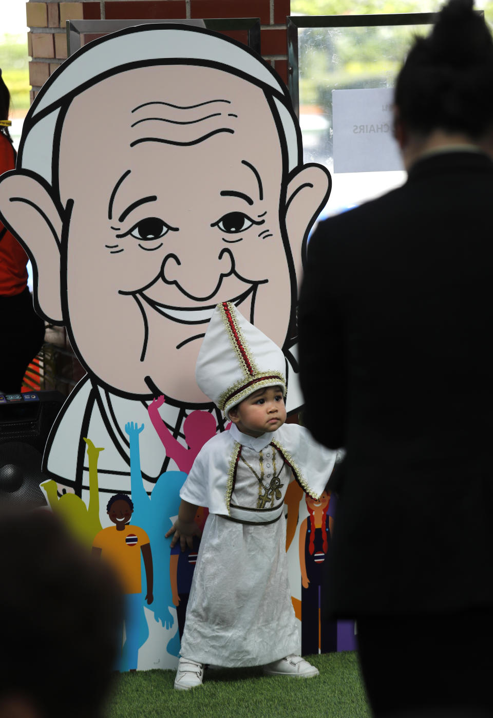 A child dressed as the Pope stands in front of a caricature of Pope Francis at Saint Louis Hospital in Bangkok, Thailand, Thursday, Nov. 21, 2019. Pope Francis called for migrants to be welcomed and for women and children to be protected from exploitation, abuse and enslavement as he began a busy two days of activities in Thailand on Thursday. (AP Photo/Manish Swarup)