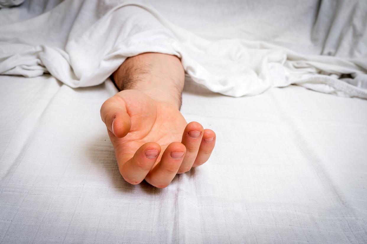 Dead man's hand under white cloth