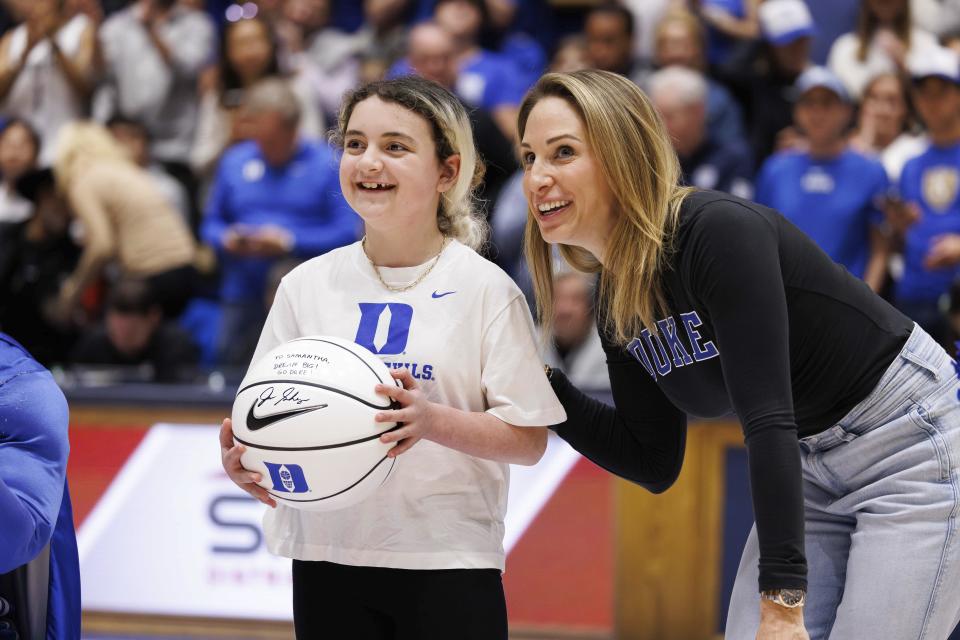 Marcelle Scheyer, right, wife of Duke coach Jon Scheyer, smiles after presenting a basketball signed by coach Scheyer to Samantha DiMartino as an honoree of the Scheyer Family Kid Captain Program, which recognizes patients and families of Duke Children's Hospital, during a timeout in an NCAA college basketball game between Duke and Louisville in Durham, N.C., Wednesday, Feb. 28, 2024. (AP Photo/Ben McKeown)