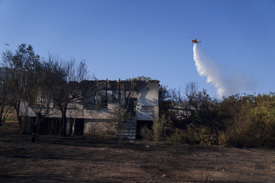 A firefighting helicopter drops water next to a burned house during a fire in Koropi suburb, eastern part of Athens, Wednesday, June 19, 2024. Scores of Greek firefighters and water-bombing aircraft were trying to contain a large wildfire on the fringes of Athens that forced authorities to issue evacuation orders Wednesday for two nearby settlements. (AP Photos/Petros Giannakouris)