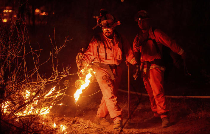 An inmate firefighter from the Trinity River Conservation Camp uses a drip torch to slow the Fawn Fire burning north of Redding, Calif. in Shasta County, on Thursday, Sept. 23, 2021. (AP Photo/Ethan Swope)