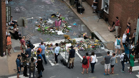 Mourners and passersby surround an impromptu memorial of flowers and chalk notes written on the street commemorating the victims at the scene of the car attack on a group of counter-protesters during the "Unite the Right" rally in Charlottesville, Virginia, August 14, 2017.