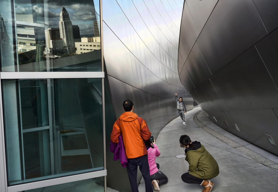 Heavy storm clouds are reflected in a window over Los Angeles City Hall, left, while Chinese tourists take photos along a walkway at the Walt Disney Concert Hall on Thursday, Dec. 26, 2019. A cold and blustery winter storm unleashed a deluge of rain and snow on Southern California, triggering tornado warnings and snarling post-Christmas travel on major routes. (AP Photo/Richard Vogel)