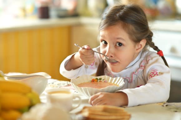 Girl eating bowl of soup at the kitchen table.