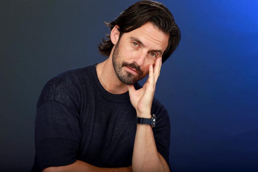 Milo Ventimiglia poses by resting his face on his opened hand, giving a slight smile