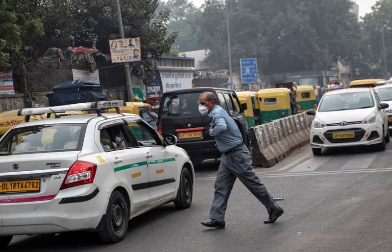A man wearing a protective mask crosses a traffic junction on a smoggy morning in New Delhi