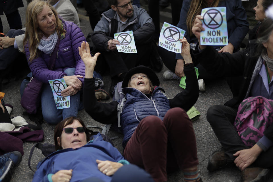 Extinction Rebellion climate change protesters block a road outside City Airport in London, Thursday, Oct. 10, 2019. Some hundreds of climate change activists are in London during a fourth day of world protests by the Extinction Rebellion movement to demand more urgent actions to counter global warming. (AP Photo/Matt Dunham)