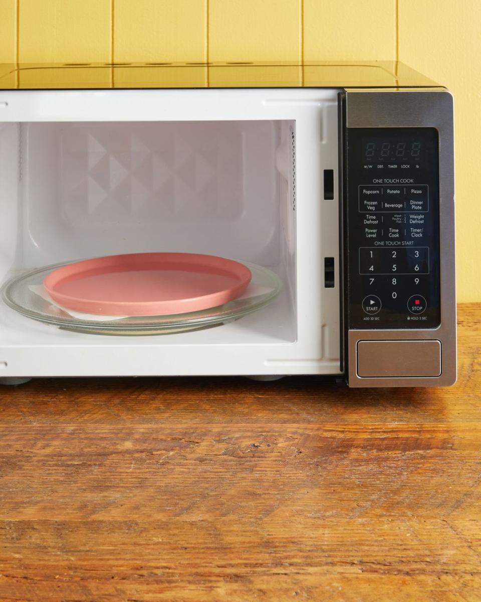 an open microwave with a pink plate set on parchment paper that has flowers in between the layers ready for drying