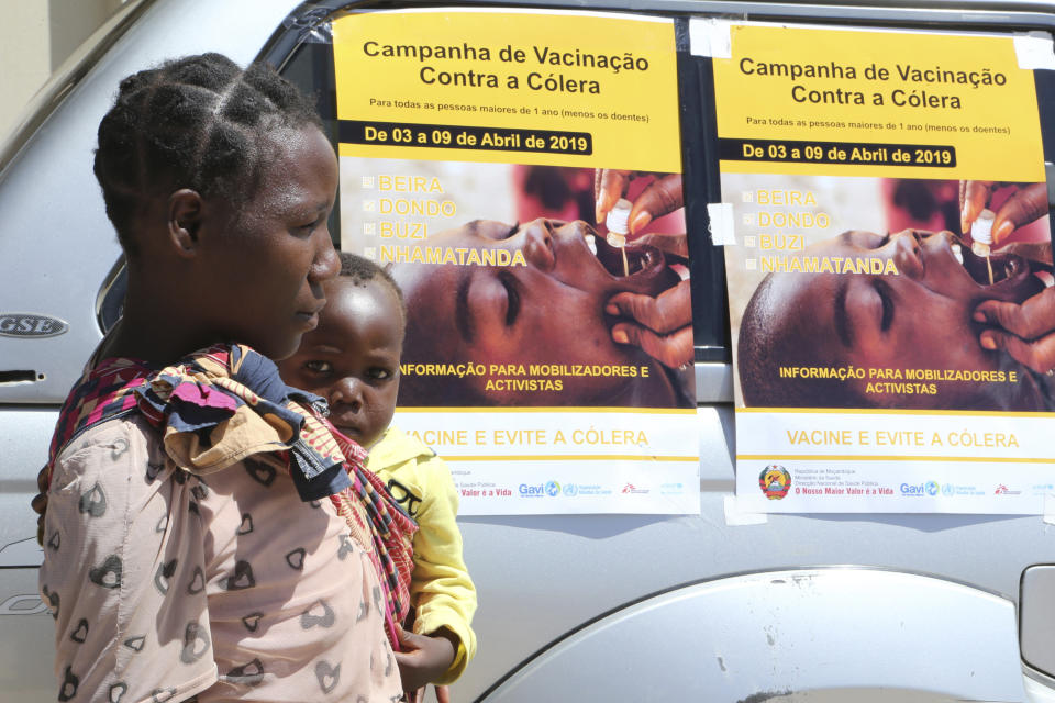 A woman and her baby walk past cholera vaccination campaign posters on the first day of the cholera vaccination programme at a camp for displaced survivors of cyclone Idai in Beira,Mozambique, Wednesday, April, 3, 2019. A cholera vaccination campaign is kicking off to reach nearly 900,000 cyclone survivors in Mozambique as officials rush to contain an outbreak of the disease. (AP Photo/Tsvangirayi Mukwazhi)