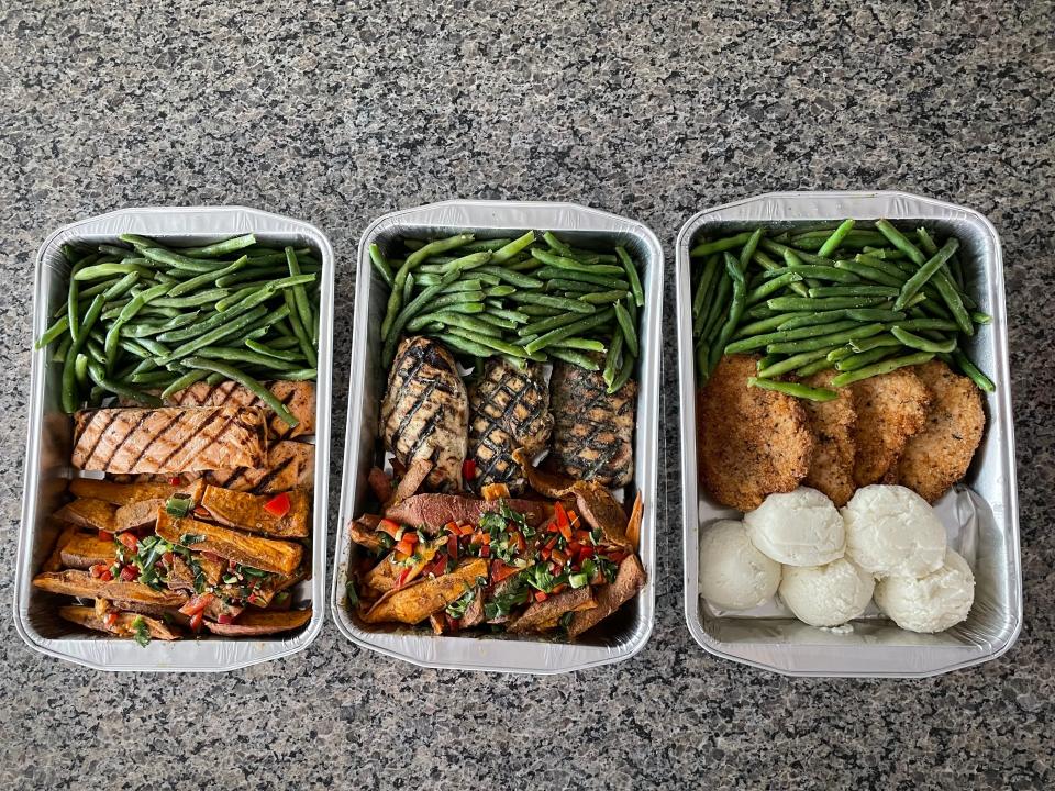 Three trees of Whole Foods meals. From left to right, tins contain salmon, potatoes, and green beans; chicken, potatoes, and green beans; breaded chicken, mashed potatoes, and green beans