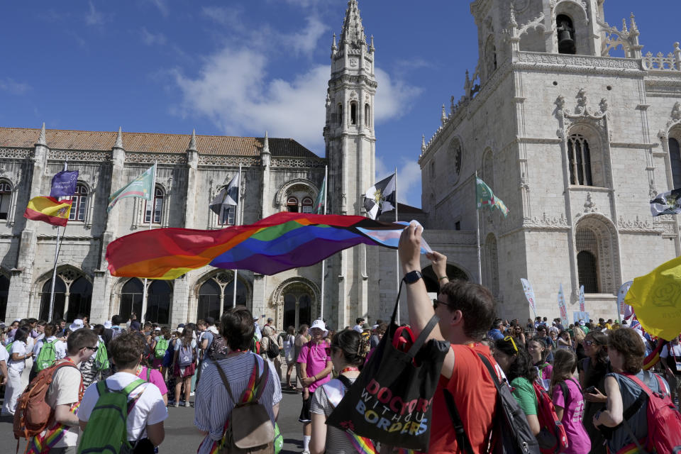 A World Youth Day pilgrim holds a Progress Pride Flag outside the 16th century Jeronimos monastery, in the background, in Lisbon, Tuesday, Aug. 1, 2023. Pope Francis will visit the monastery when he arrives Aug. 2 to attend the international event that is expected to bring hundreds of thousands of young Catholic faithful to Lisbon and goes on until Aug. 6. (AP Photo/Ana Brigida)