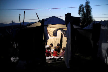 Two migrant men and four babies sit inside a tent at a makeshift camp next to the Moria camp for refugees and migrants on the island of Lesbos, Greece, September 18, 2018. Picture taken September 18, 2018. REUTERS/Giorgos Moutafis