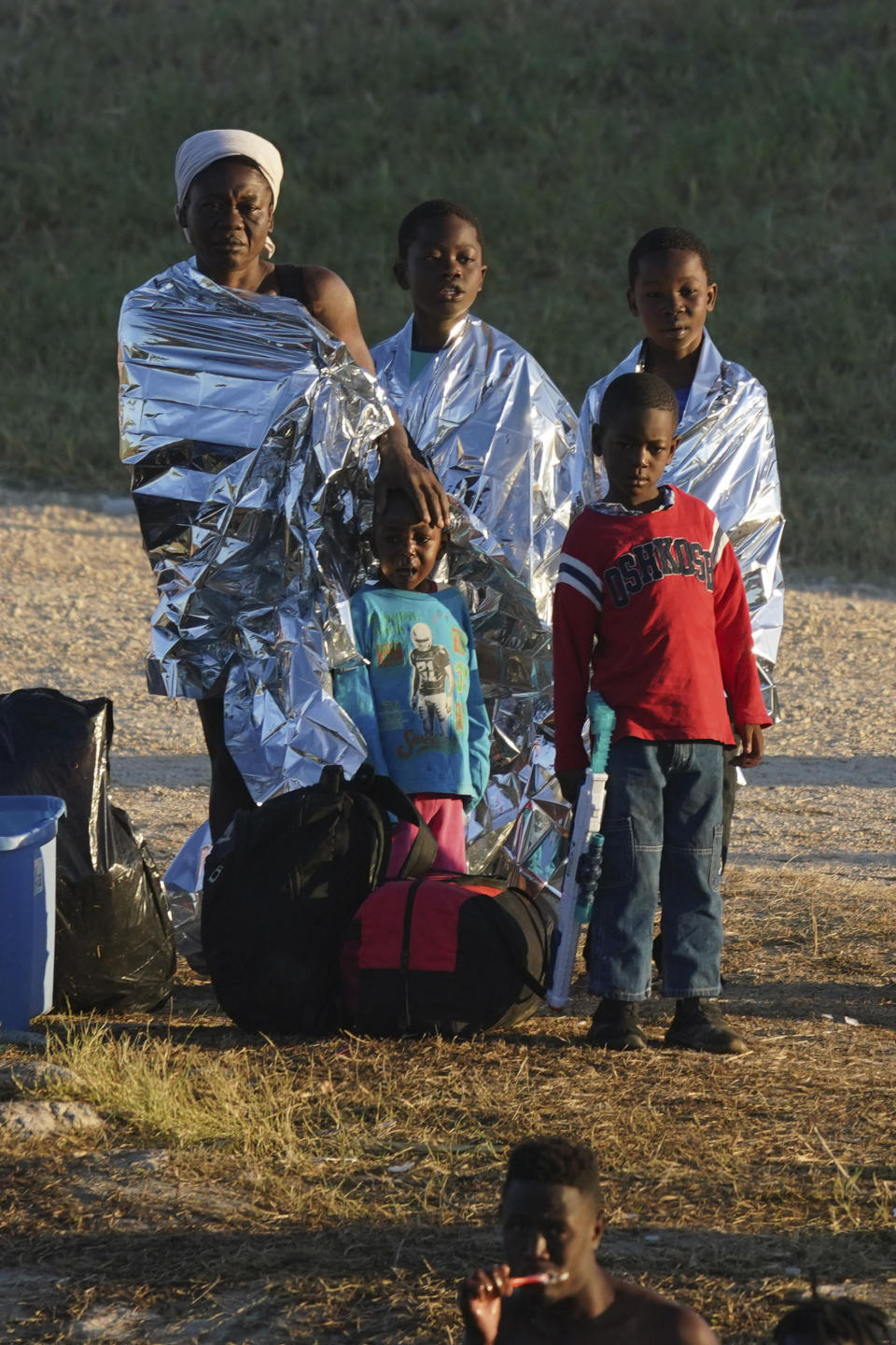 A migrant family stands on the U.S. side of the Rio Grande river where another migrant brushes his teeth, after they crossed the border to Del Rio, Texas, from Ciudad Acuna, Mexico, early Thursday, Sept. 23, 2021. (AP Photo/Fernando Llano)