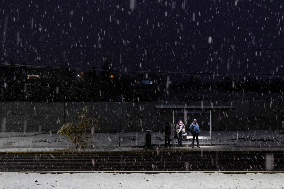 People wait for public transport at a bus stop in the middle of a snowfall, in Santiago, Chile, Tuesday, May 7, 2024. (AP Photo/Matias Basualdo)