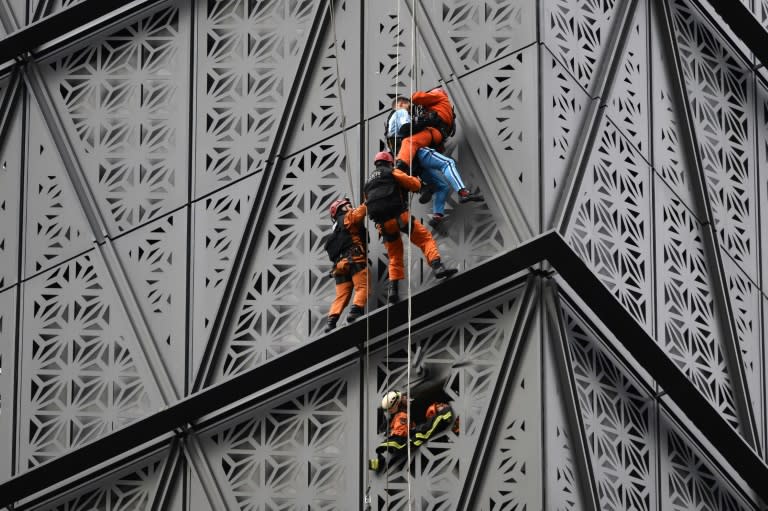 Los bomberos interceptan al escalador polaco Marcin Banot (2do-derecha) mientras subía a un edificio en Puerto Madero vistiendo una camiseta de la selección argentina de fútbol con el número 10 de Lionel Messi en Buenos Aires el 11 de junio de 2024. (LUIS ROBAYO)