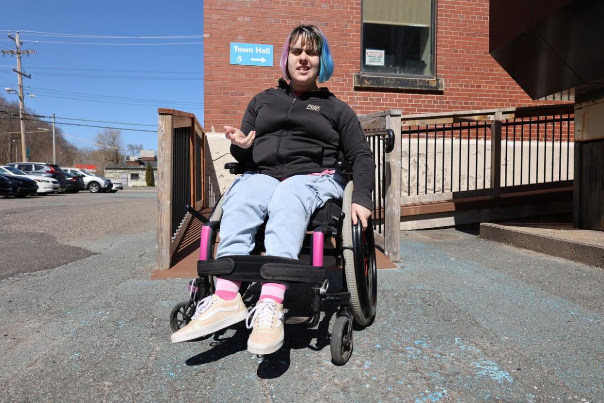 Hannah Corkum poses at the rear entrance to the Kentville town hall. The incline of the wooden ramp is difficult for her to navigate in her wheelchair and a lip at the door prevents her from getting inside without help. Corkum is an Annapolis Valley resident and athlete who helped Kentville conduct an accessibility audit in Oct. 2023.   (Jerry West/CBC - image credit)