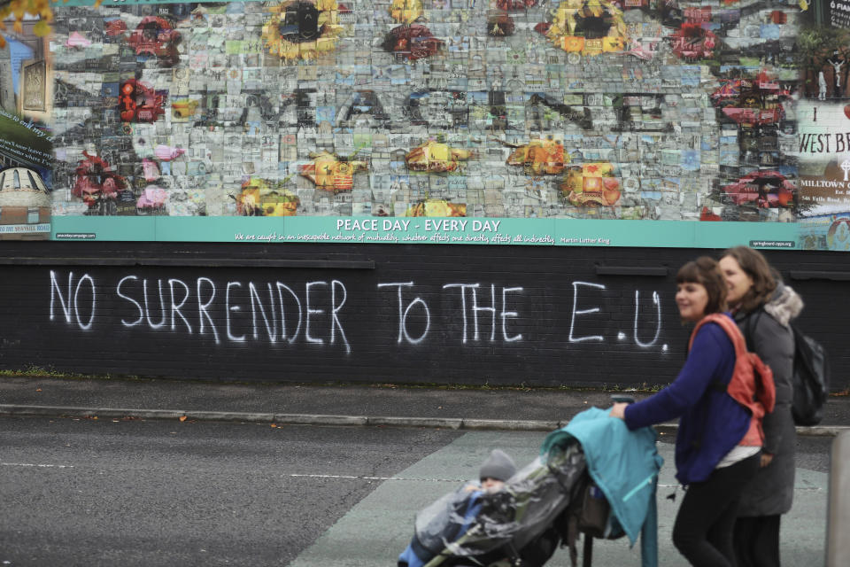 In this photo dated Monday Oct. 14, 2019 people walk past pro-Brexit graffiti in West Belfast Northern Ireland. Fears about a return to the violence that killed more than 3,500 people over three decades have made Northern Ireland the biggest hurdle for U.K. and EU officials who are trying to hammer out a Brexit divorce deal. (AP Photo/Peter Morrison)