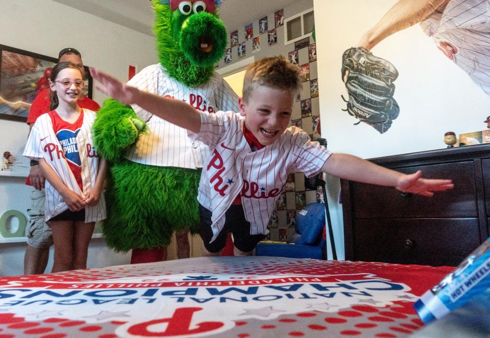 Rowan Linder, a 5 year-old big-time baseball fan who is battling cancer, jumps on his bed after seeing his bedroom redecorated by members of the Philadelphia Phillies front office as his sister Aubrey (9) and father, Gary, left, watch alongside the Phillie Phanatic in Middletown on Thursday, Sept. 7, 2023.

[Daniella Heminghaus | Bucks County Courier Times]