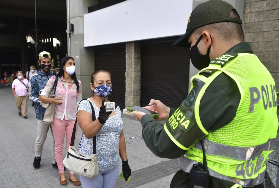 In this June 8, 2020 photo, a police officer uses a newly developed software to scan the identification card which determines if a resident has the authorization to be out in public, amid the new coronavirus pandemic, in Medellin, Colombia. Critics of the city’s mayor fear the immense data being collected on citizens amounts to a severe invasion of privacy, but even they admit that it has proven effective in containing COVID-19. (AP Photo/Luis Benavides)