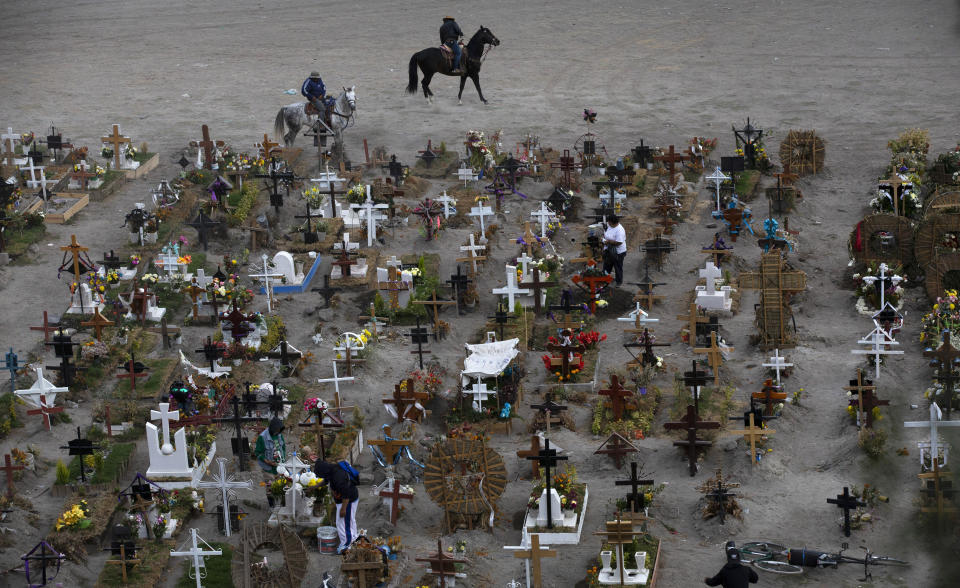 FILE - In this Nov. 18, 2020 file photo, workers ride their horses in the Valle de Chalco municipal cemetery, mostly reserved for those who have died from the coronavirus, on the outskirts of Mexico City. As Mexico approaches 200,000 in officially test-confirmed deaths from COVID-19, the real death toll is probably higher due to the country’s extremely low rate of testing. (AP Photo/Marco Ugarte, File)