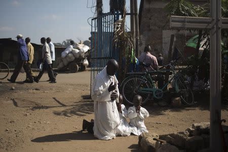 A member of the Legio Maria and his children pray by a cross near the gate of their church during Sunday mass in Korogocho, Nairobi, Kenya, July 5, 2015. REUTERS/Siegfried Modola