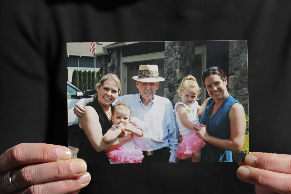 In this Wednesday, April 8, 2020, photo, Kelly Adsero holds a family photo of her grandfather Bill Chambers, center, as he stands with Adsero, right, her daughter Molly, and Adsero's sister Kristi Mandich, left, and her daughter Guiliana. Chambers, 97, died March 14, 2020, at an adult family home where he lived with four other World War II veterans. He wasn't obviously ill, but tested positive for the new coronavirus after he died. (AP Photo/Ted S. Warren)