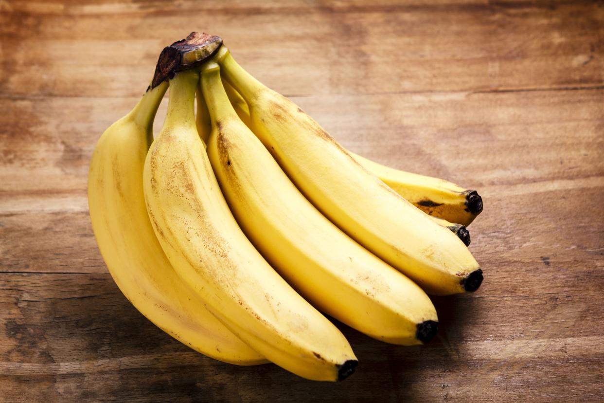 A hand of ripe, yellow bananas on a wooden table