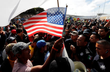 A migrant, part of a caravan of thousands traveling from Central America en route to the United States, holds a U.S. flag as the group of migrants negotiate with Mexican policemen during their gathering near the El Chaparral port of entry of border crossing between Mexico and the United States in Tijuana, Mexico November 22, 2018. REUTERS/Kim Kyung-Hoon