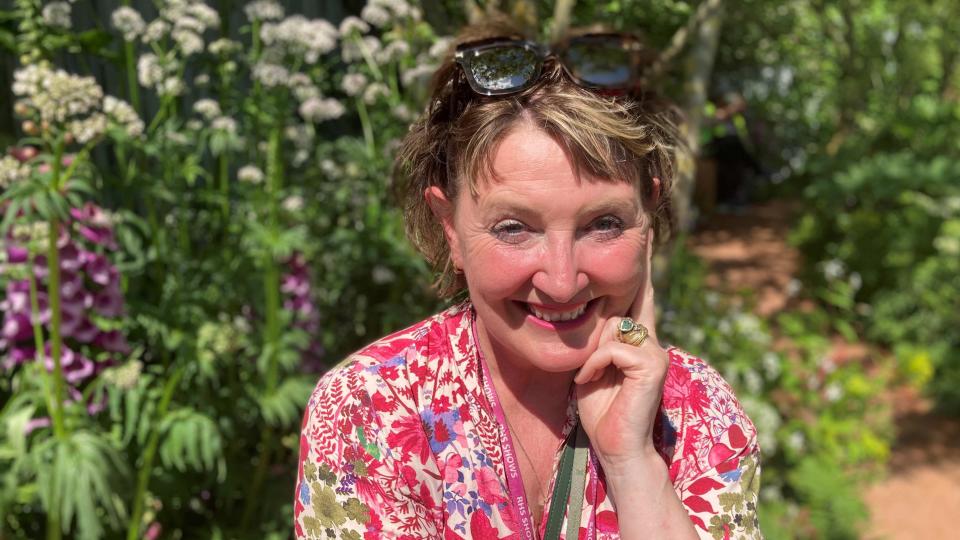 Ann-Marie Powell smiling into the camera with beautiful flowers behind her