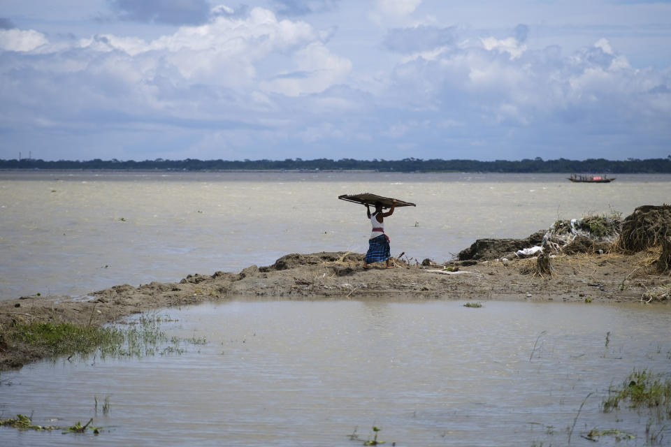 A person carries a corrugated sheet to shift their house because of erosion due to the Meghna River in the Ramdaspur village in the Bhola district of Bangladesh on July 5, 2022. Mohammad Jewel and Arzu Begum were forced to flee the area last year when the river flooded and destroyed their home. (AP Photo/Mahmud Hossain Opu)