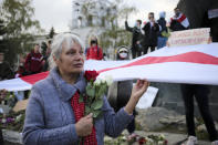 A woman holds red and white roses and an old Belarusian national flags during an opposition rally to protest the official presidential election results in Minsk, Russia, Monday, Oct. 26, 2020. Factory workers, students and business owners in Belarus have started a general strike, calling for authoritarian President Alexander Lukashenko to resign after more than two months of mass protests triggered by a disputed election. (AP Photo)