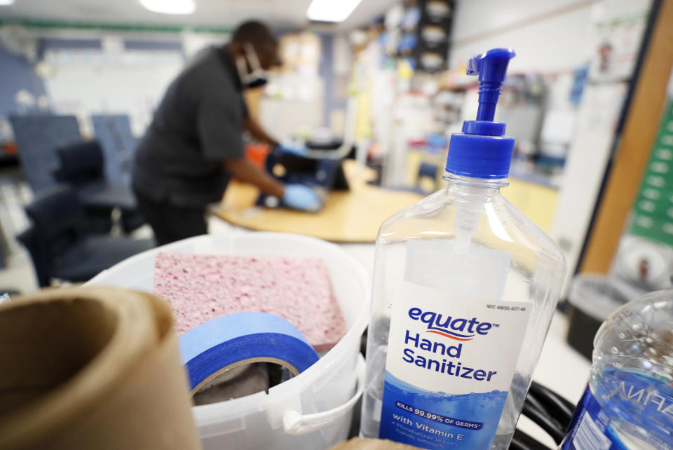 A bottle of hand sanitizer sits on a cart as Des Moines Public Schools custodian Tracy Harris cleans a chair in a classroom at Brubaker Elementary School, Wednesday, July 8, 2020, in Des Moines, Iowa. School districts that plan to reopen classrooms in the fall are wrestling with whether to require teachers and students to wear face masks. In Iowa, among other places, where Democratic-leaning cities like Des Moines and Iowa City have required masks to curb the spread of the coronavirus, while smaller, more conservative communities have left the decision to parents. (AP Photo/Charlie Neibergall)