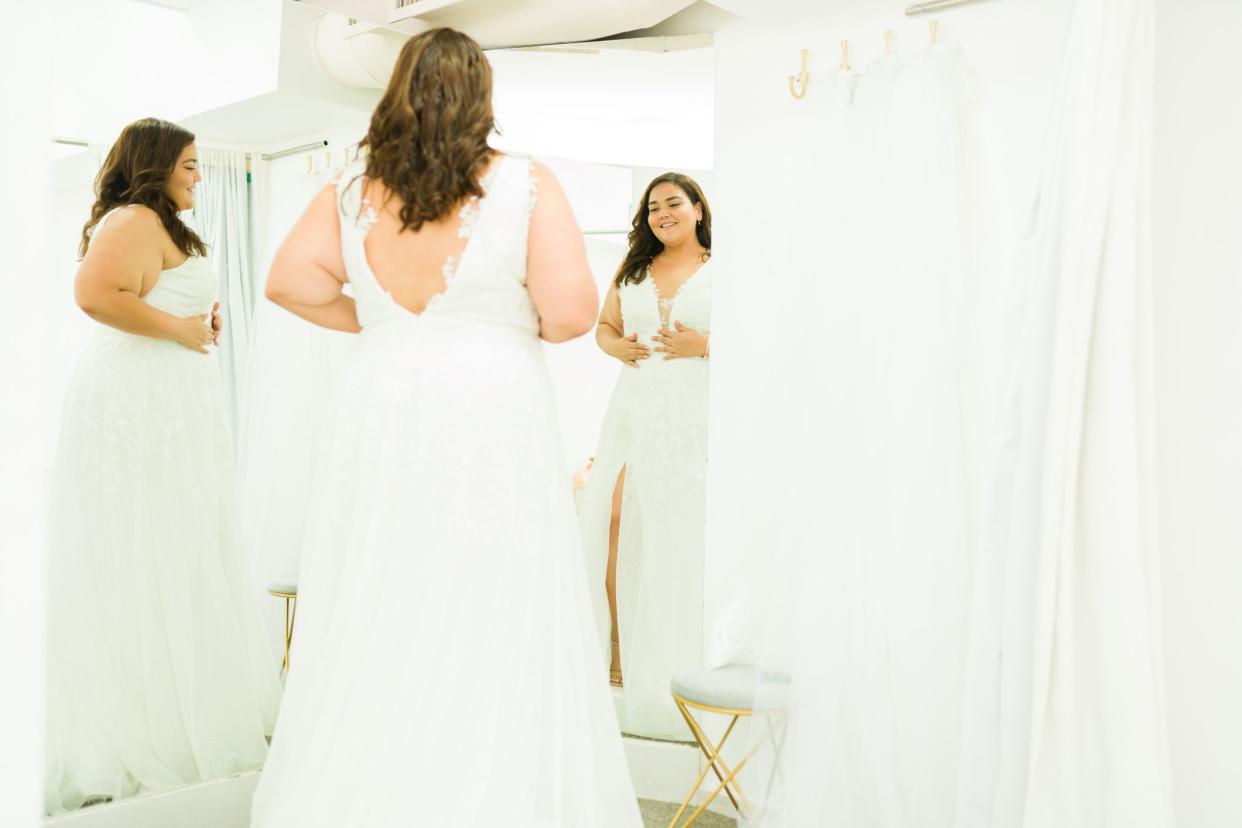 Obese young woman smiling looking in the mirror while shopping for a wedding dress