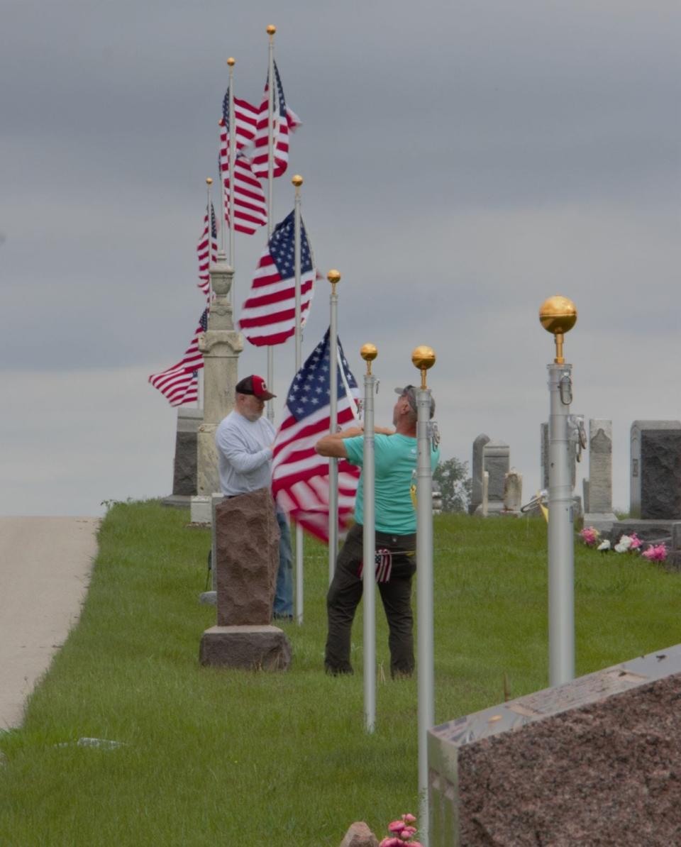 Jim McCormick on the left and Galen Stole raise flags at the Roland cemetery prior to a Memorial Day event there.