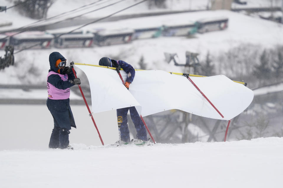 Course staff hold a banner from being blown away by bad weather as they wait for confirmation if the men's slalom competition will take place during the FIS Alpine Ski World Cup at Naeba Ski Resort in Yuzawa, Niigata prefecture, northern Japan, Sunday, Feb. 23, 2020. (AP Photo/Christopher Jue)