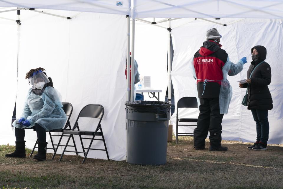 A worker, left, rests for a second between patients, as another person, right, is tested for COVID-19 at a walk-up testing site at Farragut Square, Thursday, Dec. 23, 2021, just blocks from the White House in Washington. (AP Photo/Jacquelyn Martin)