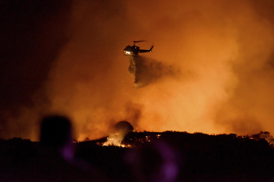 A helicopter drops water on a brushfire in the Santa Monica Mountains in Newbury Park, Calif., Oct. 10, 2019. (Photo: Michael Owen Baker/AP)